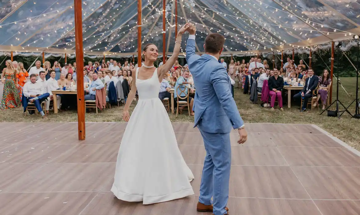 Bride & groom dancing on a dark wood dance floor under Coastal Clear Tent