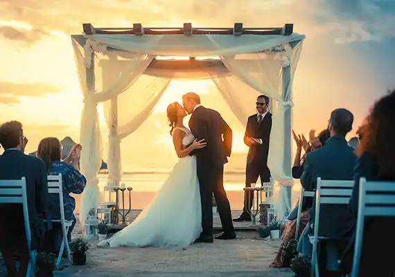 Couple getting married, kissing, guests clapping, sunset in background